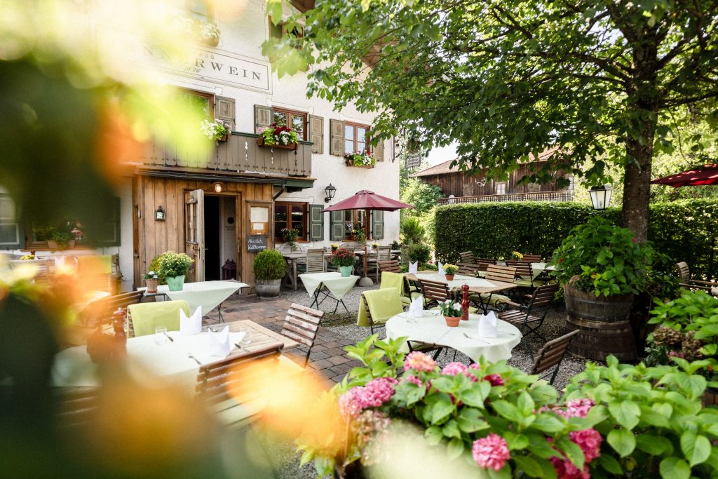 Idyllischer Biergarten mit gedeckten Tischen, Blumenarrangements und traditioneller Hausfassade im Jennerwein Gasthaus